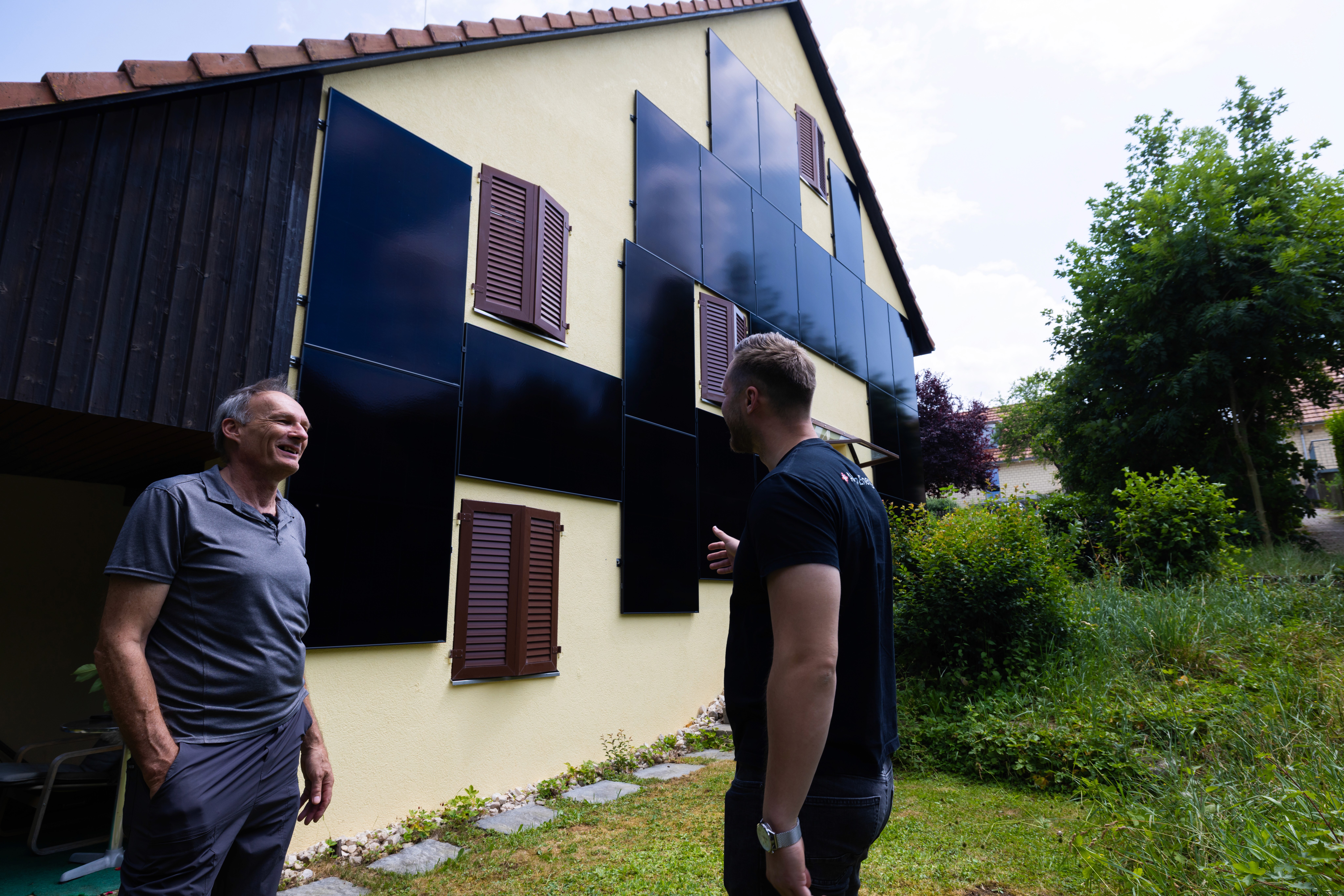 Kunde und AlpenEnergie-Monteur im Gespräch vor einer Fassade mit senkrecht montierten Solarmodulen
