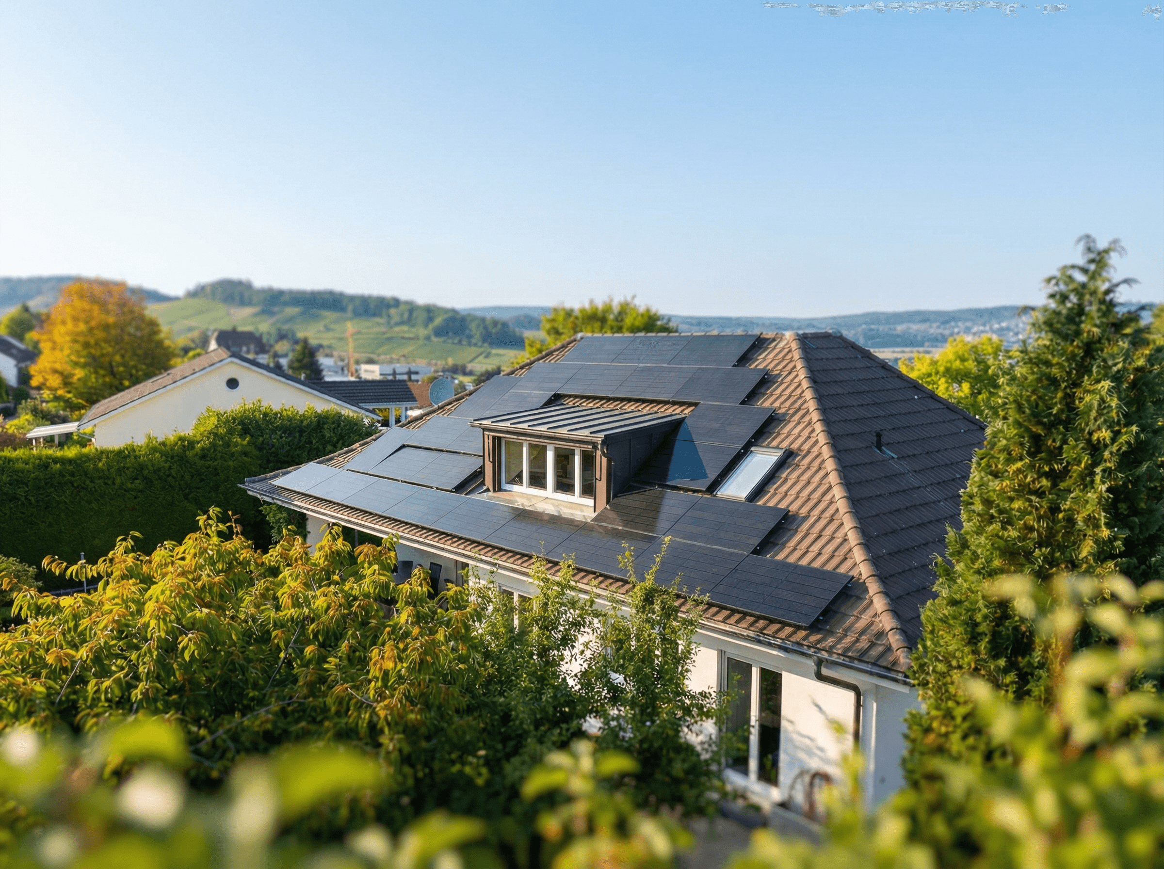 Einfamilienhaus mit schwarzen Solarmodulen rund um die Dachgaube, dahinter Rebhänge
