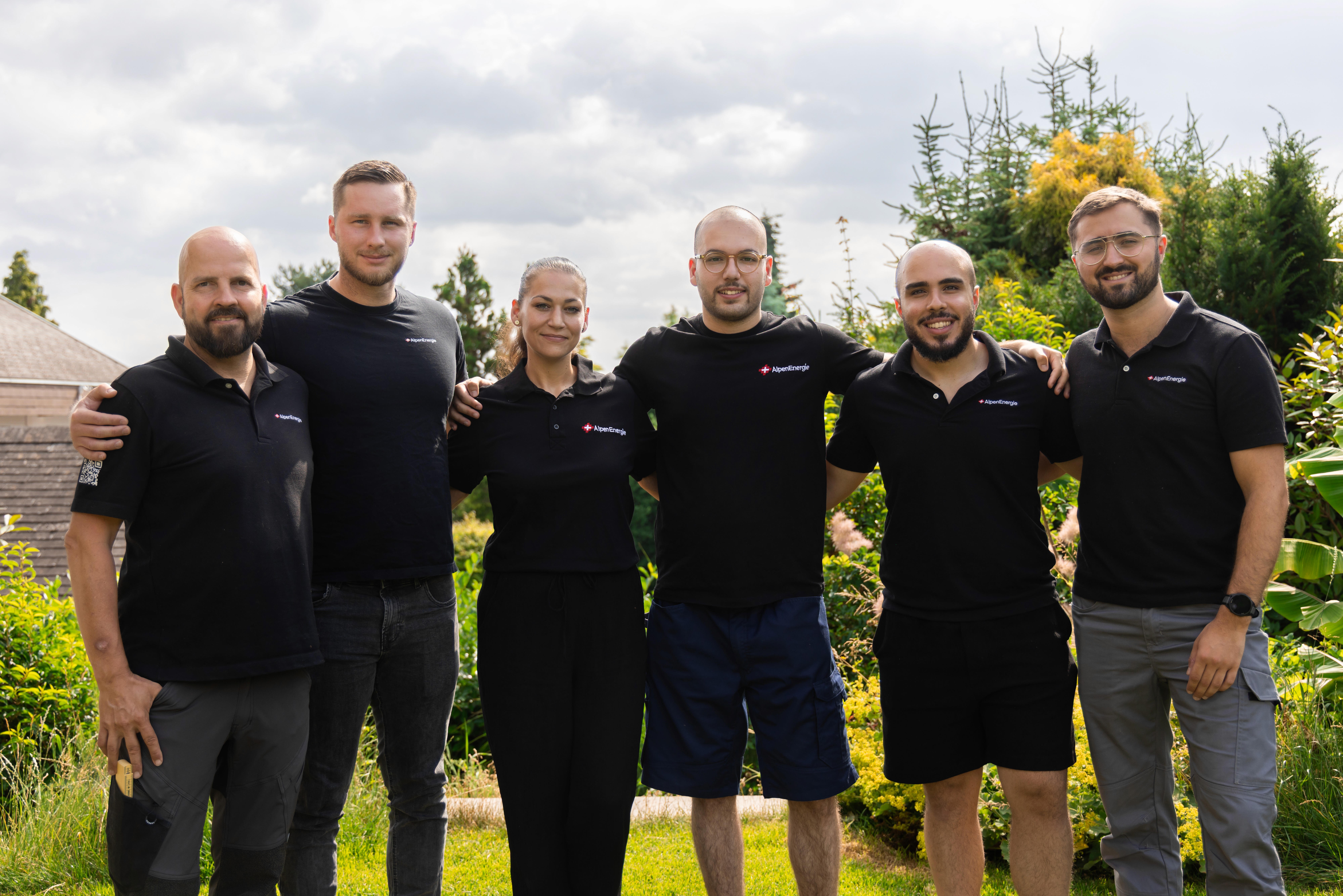 Das AlpenEnergie-Team in schwarzen Polohemden nebeneinander im Garten
